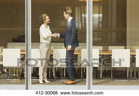 Businessman and businesswoman handshaking at conference room window View Large Photo Image Stock Photo - Businessman and businesswoman handshaking at conference room window. Fotosearch