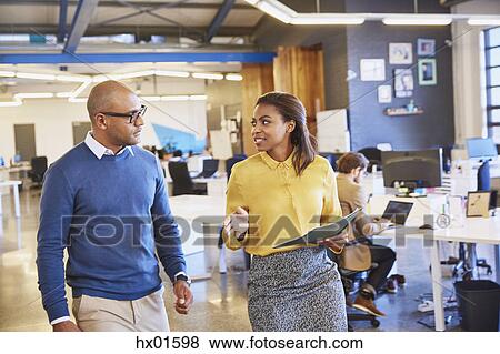 Stock Photo - Businessman and businesswoman walking and talking in office. Fotosearch