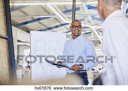 Stock Photograph - Businessman at flipchart leading meeting in conference room. Fotosearch