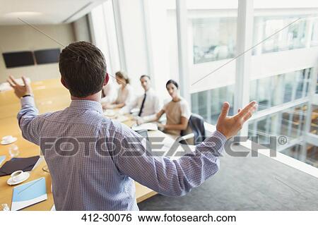 Stock Photograph - Businessman gesturing to colleagues in conference room meeting. Fotosearch