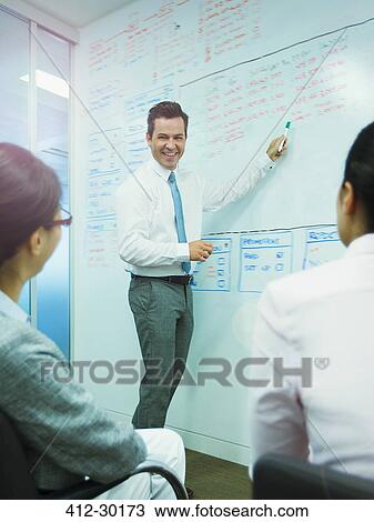 Stock Image - Businessman leading meeting at whiteboard in conference room. Fotosearch