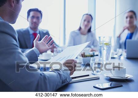 Businessman leading meeting explaining paperwork in conference room View Large Photo Image Stock Photo - Businessman leading meeting explaining paperwork in conference room. Fotosearch