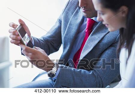 Stock Image - Businessman showing cell phone video to businesswoman. Fotosearch