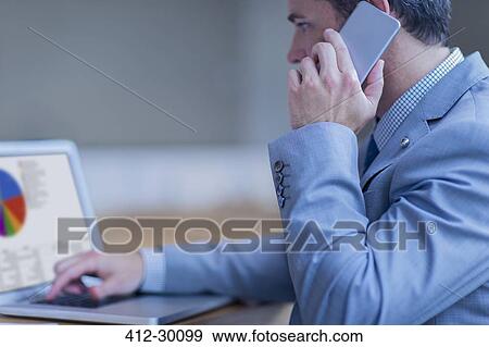 Businessman talking on cell phone and working at laptop View Large Photo Image Stock Photo - Businessman talking on cell phone and working at laptop. Fotosearch