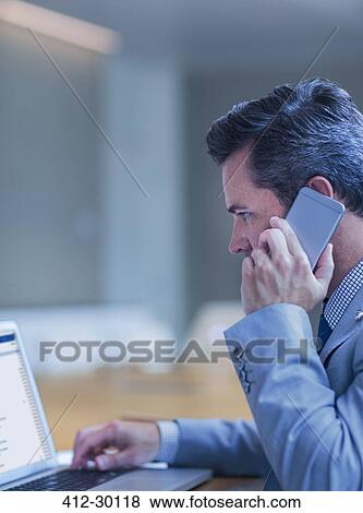 Businessman talking on cell phone and working at laptop in conference room View Large Photo Image Stock Photo - Businessman talking on cell phone and working at laptop in conference room. Fotosearch