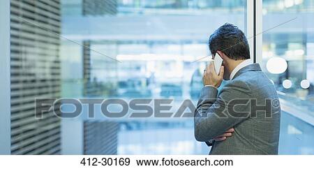 Stock Photo - Businessman talking on cell phone at office window. Fotosearch