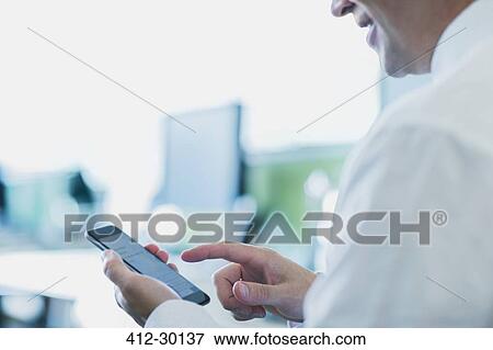 Stock Photo - Businessman using cell phone in office. Fotosearch