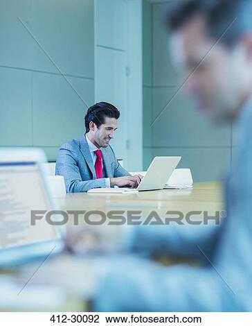 Stock Image - Businessman working at laptop in conference room. Fotosearch