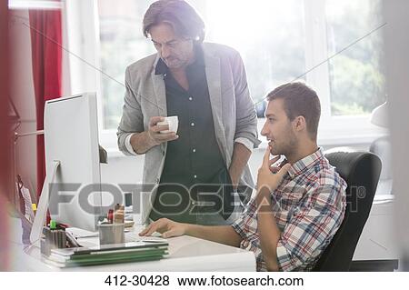 Stock Photo - Businessmen drinking coffee and working at computer in office. Fotosearch