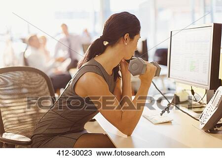 Businesswoman doing biceps curls with dumbbell and talking on telephone at computer in office View Large Photo Image Stock Image - Businesswoman doing biceps curls with dumbbell and talking on telephone at computer in office. Fotosearch