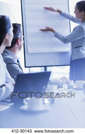 Businesswoman explaining graph at flip chart in conference room meeting View Large Photo Image Stock Image - Businesswoman explaining graph at flip chart in conference room meeting. Fotosearch
