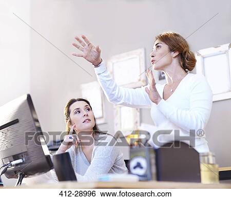 Stock Photograph - Businesswoman gesturing and explaining to coworker at computer. Fotosearch