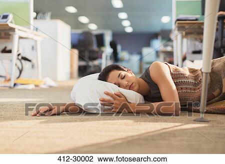 Stock Image - Businesswoman sleeping with pillow on office floor. Fotosearch