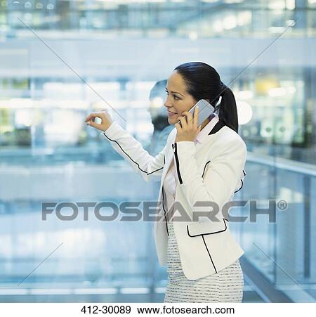 Stock Photo - Businesswoman talking on cell phone at office window. Fotosearch