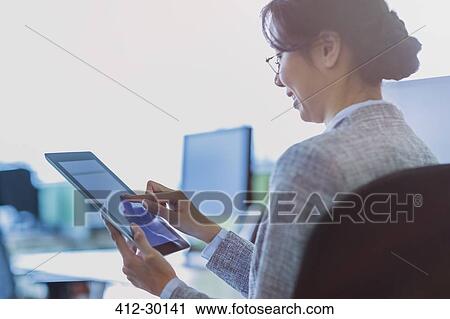 Stock Image - Businesswoman using digital tablet in office. Fotosearch
