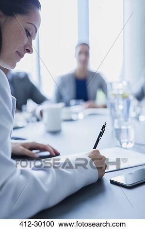 Stock Image - Businesswoman writing on paperwork in conference room meeting. Fotosearch