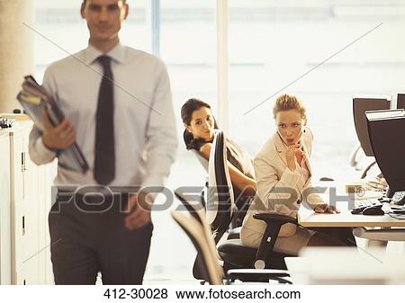 Stock Photo - Businesswomen checking out passing businessman in office. Fotosearch