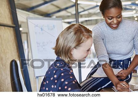 Businesswomen discussing paperwork in conference room meeting View Large Photo Image Stock Photo - Businesswomen discussing paperwork in conference room meeting. Fotosearch