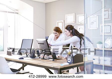 Stock Photo - Businesswomen talking at computer in office. Fotosearch