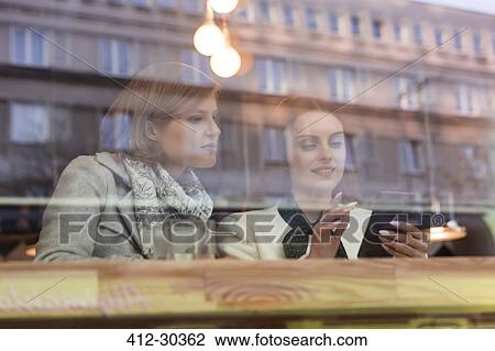 Stock Image - Businesswomen using cell phone at cafe window. Fotosearch