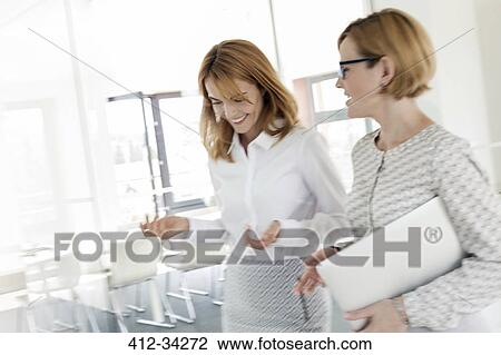 Businesswomen walking and talking in office View Large Photo Image Stock Image - Businesswomen walking and talking in office. Fotosearch