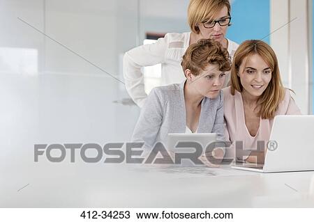 Businesswomen working at laptop and digital tablet in conference room meeting View Large Photo Image Stock Image - Businesswomen working at laptop and digital tablet in conference room meeting. Fotosearch