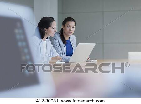 Stock Image - Businesswomen working at laptop in conference room. Fotosearch