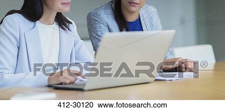 Stock Image - Businesswomen working at laptop in conference room. Fotosearch