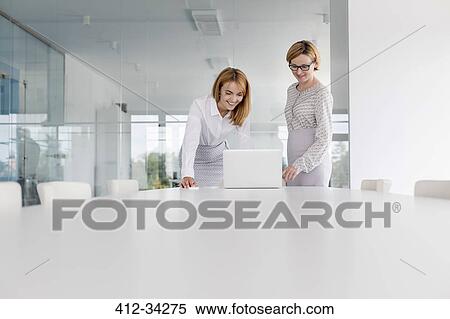 Stock Photography - Businesswomen working at laptop in conference room. Fotosearch