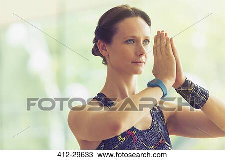 Stock Image - Calm woman with hands at prayer position in yoga class. Fotosearch