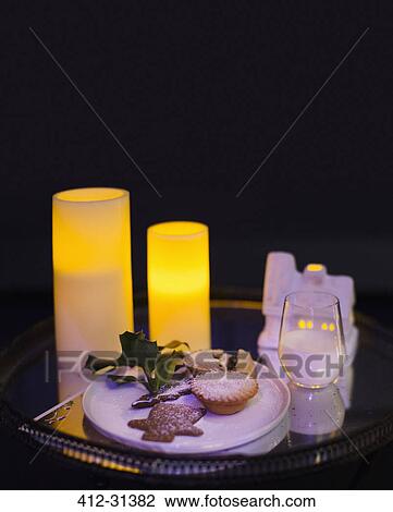 Stock Image - Candles illuminating Christmas cookies and milk left for Santa. Fotosearch