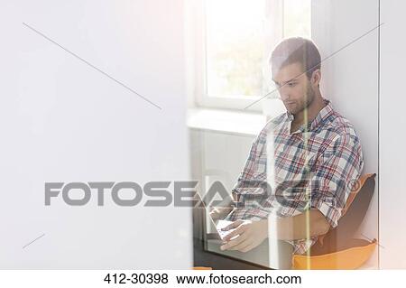 Stock Photo - Casual businessman using laptop in office window. Fotosearch