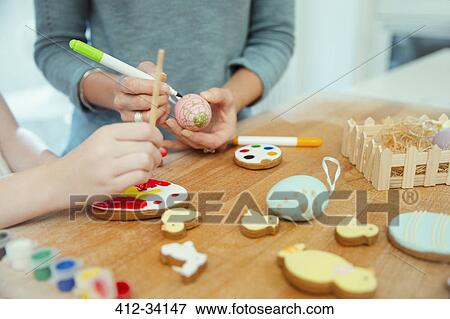 Stock Photo - Close up mother and daughter decorating Easter eggs and cookies. Fotosearch