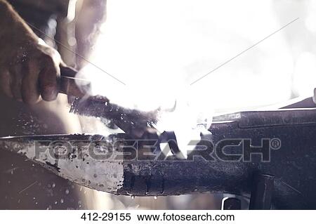 Stock Photography - Close up of blacksmith brushing iron tool over anvil in forge. Fotosearch