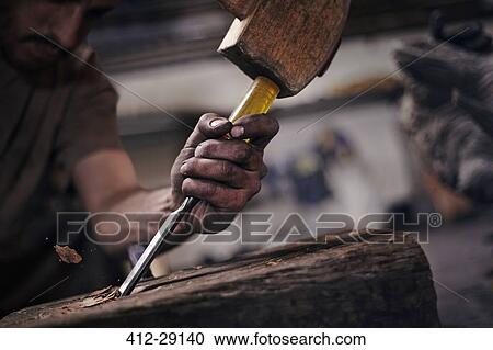 Stock Image - Close up of blacksmith chiseling wood with tool. Fotosearch