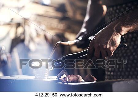 Stock Image - Close up of blacksmith heating metal with blowtorch in forge. Fotosearch