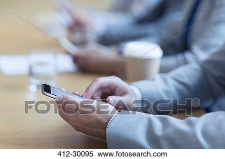 Stock Photography - Close up of businessman using cell phone in meeting. Fotosearch