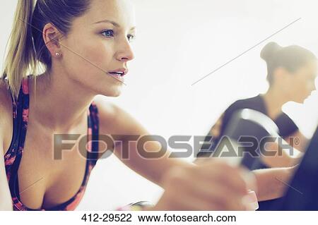 Stock Image - Close up of focused woman riding exercise bike at gym. Fotosearch