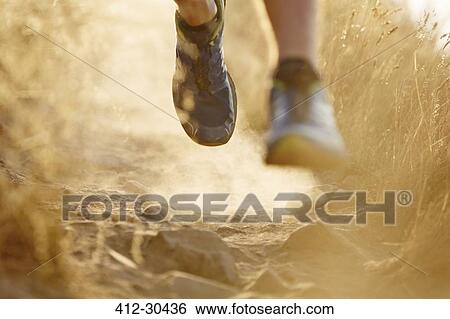Stock Photograph - Close up of runners feet on dirt trail. Fotosearch