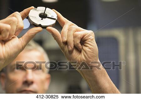 Stock Photography - Close up of worker examining part in steel factory. Fotosearch