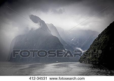 Stock Image - Clouds and fog surrounding cliffs, Milford Sound, South Island New Zealand. Fotosearch