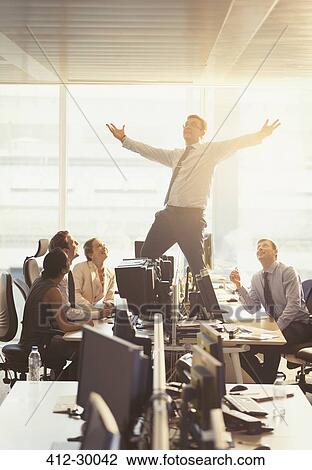 Colleagues watching exuberant businessman celebrating on top of desks in office View Large Photo Image Stock Image - Colleagues watching exuberant businessman celebrating on top of desks in office. Fotosearch
