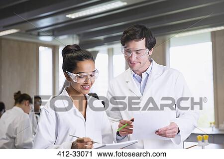 Stock Image - College students in lab coats discussing notes in science laboratory classroom. Fotosearch