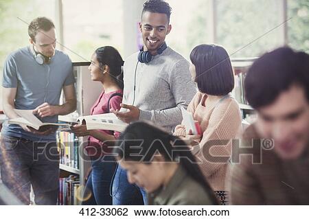 Stock Image - College students talking and studying in library. Fotosearch