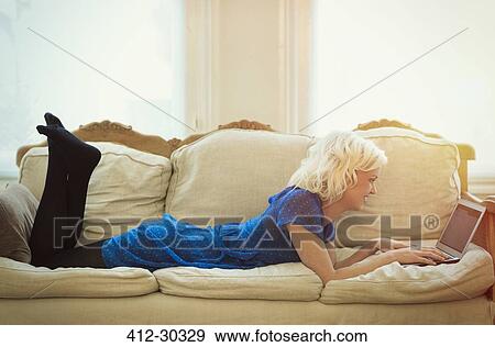 Comfortable woman using laptop on living room sofa View Large Photo Image Stock Photo - Comfortable woman using laptop on living room sofa. Fotosearch