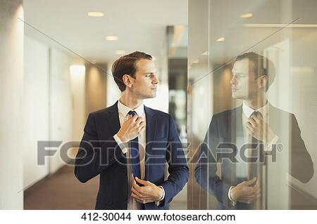 Confident businessman adjusting tie in office corridor View Large Photo Image Picture - Confident businessman adjusting tie in office corridor. Fotosearch