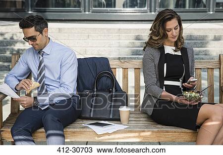 Stock Image - Corporate businessman and businessman working and eating lunch on bench. Fotosearch