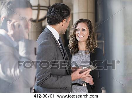 Stock Image - Corporate businessman and businesswoman with digital tablet talking. Fotosearch