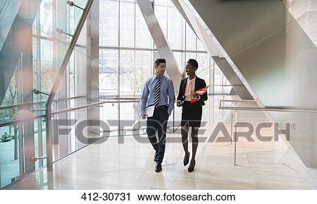 Stock Image - Corporate businessman and businesswoman walking and talking in modern office lobby. Fotosearch