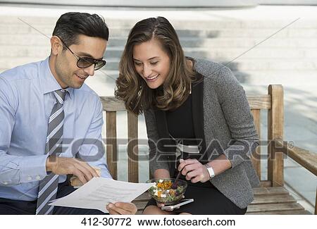 Corporate businessman and businesswoman eating lunch and reviewing paperwork on bench View Large Photo Image Stock Image - Corporate businessman and businesswoman eating lunch and reviewing paperwork on bench. Fotosearch